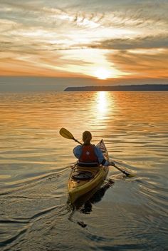 a person in a kayak paddling on the water at sunset