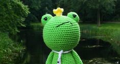 a crocheted frog with a yellow crown on its head sitting in front of a pond