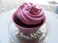 a pink frosted cupcake sitting on top of a glass plate