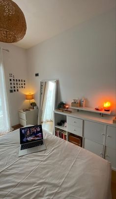 an open laptop computer sitting on top of a bed next to a lamp and dresser