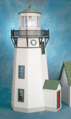 a paper model of a lighthouse with two small houses next to it on a blue background