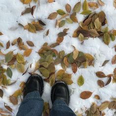 a person standing in the snow with their feet up and leaves scattered on the ground