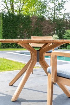 a wooden table sitting on top of a patio next to a swimming pool and trees