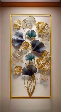 an art piece with gold and blue leaves on the wall in front of a white background