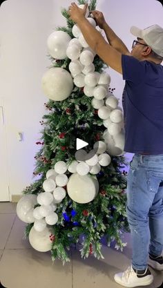 a man is decorating a christmas tree with white balloons