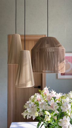 three lamps hanging from the ceiling above a table with flowers in vases on it