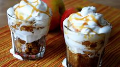 two desserts are sitting on a table with apples in the background and one is topped with whipped cream