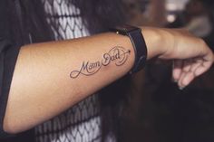 a woman with a tattoo on her arm that says mom and dad in cursive font