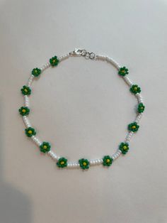 a green and white beaded bracelet with flowers on it's end, sitting on a table