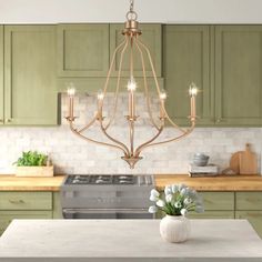 a chandelier hanging from the ceiling in a kitchen with green cabinets and white countertops