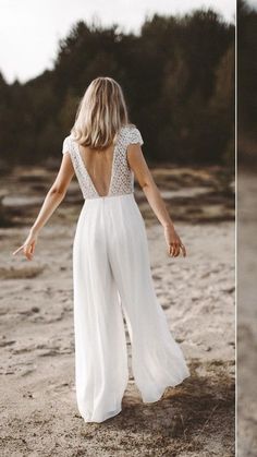 a woman standing in the sand with her back to the camera and wearing a white jumpsuit