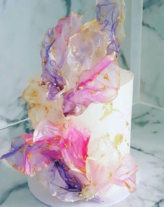 a white cake with pink and purple flowers on it sitting on a marble counter top