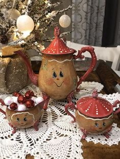 three ceramic teapots on a doily next to a christmas tree with ornaments