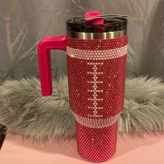 a red and silver coffee cup with a football design on the side, sitting on a pink tablecloth