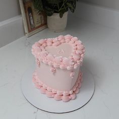 a pink heart shaped cake sitting on top of a white plate next to a potted plant