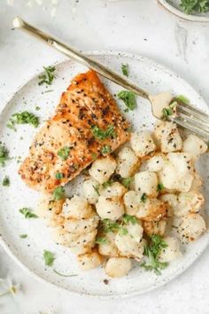 a white plate topped with chicken and cauliflower covered in seasoning next to a fork