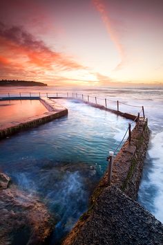 the sun is setting over the ocean with waves coming in to shore and people standing on the pier