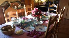 the table is set for christmas dinner with plates and bowls on it, along with candles