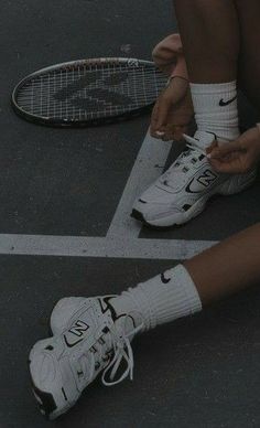 a person tying their tennis shoes on the ground next to a racquet and racket