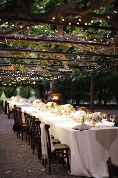 a long table is set with white linens and lights strung from the ceiling above it