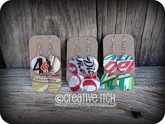 three earrings with different designs on them sitting next to each other in front of a wooden background