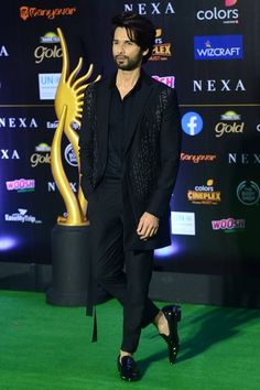 man in black suit walking on green carpet with award statue at awards ceremony, india