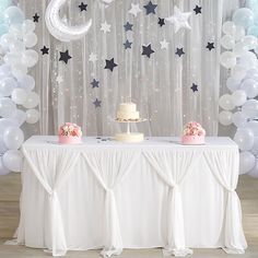 a white table topped with a cake next to balloons and stars on the wall behind it