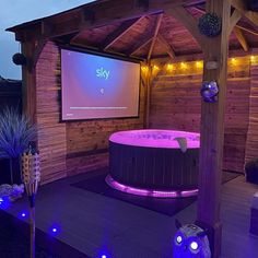 an outdoor hot tub with projection screen and blue lights on the sides, in front of a wooden gazebo