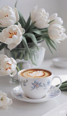 a cup of cappuccino on a saucer next to some white tulips