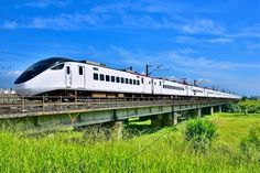 a white train traveling over a bridge next to tall grass and power lines in the background