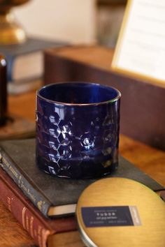 a blue glass cup sitting on top of a wooden table next to a stack of books