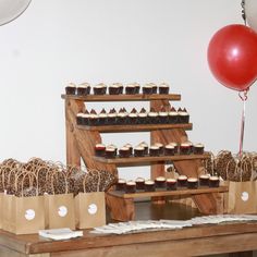 a table topped with lots of cupcakes next to a red balloon and some brown paper bags