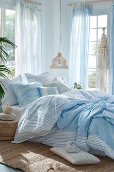 a bed with blue sheets and pillows in a room next to windows, rugs and potted plants