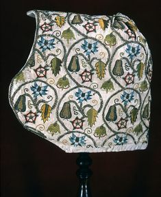 a lamp shade that has been decorated with flowers and leaves on white fabric, sitting on a black stand