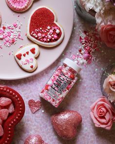 valentine's day cookies and other treats on a table with pink flowers, heart - shaped sugars and sprinkles