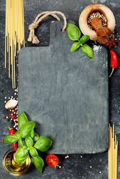 a slate board surrounded by pasta, basil and other ingredients on a dark background with space for text