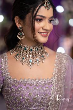 a woman in a purple dress with jewelry on her neck and headpiece, smiling at the camera