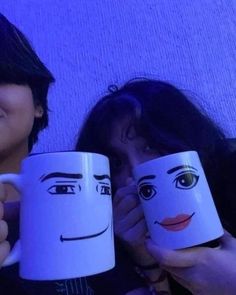 two women holding mugs with faces drawn on them