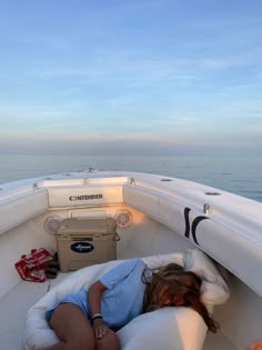 a woman laying on top of a white couch in the back of a boat near the ocean