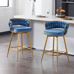 two blue velvet bar stools in front of a white countertop with gold legs