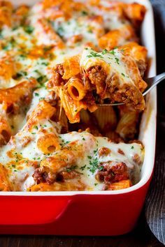 a red casserole dish with meat and cheese on it, being lifted by a fork