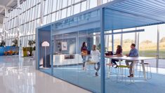 three people are sitting at a table in an open room with glass walls and blue flooring