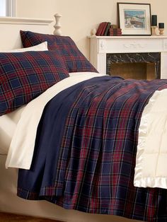 a bed with blue and red plaid comforter next to a fireplace