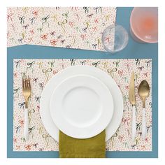 a place setting with white plates and silverware on a blue table cloth, next to utensils