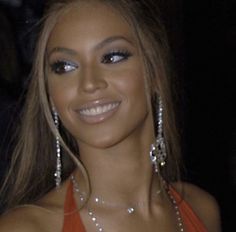 a woman in an orange dress with large silver earrings on her head and one eye open