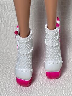 a close up of a doll's feet wearing white and pink shoes with pearls on them