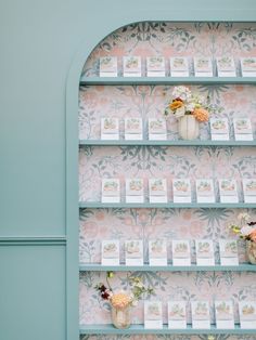 there are many flowers in vases on the wall behind this display case that is filled with greeting cards