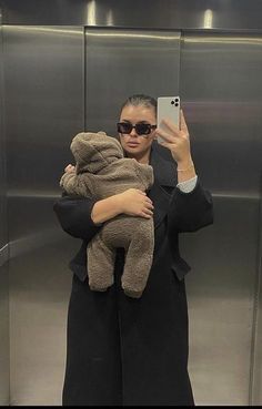 a woman taking a selfie in an elevator with a teddy bear on her arm