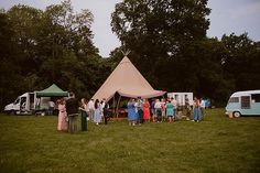 a group of people standing in front of a teepee tent on top of a lush green field