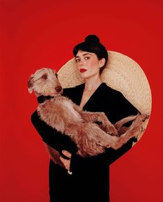 a woman holding a dog in her arms with a straw hat on top of her head